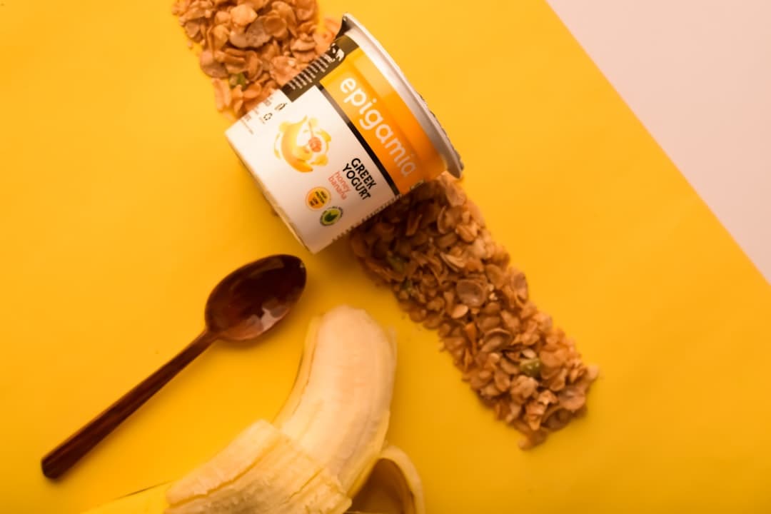 Yogurt cup with granola, banana, and spoon on yellow background